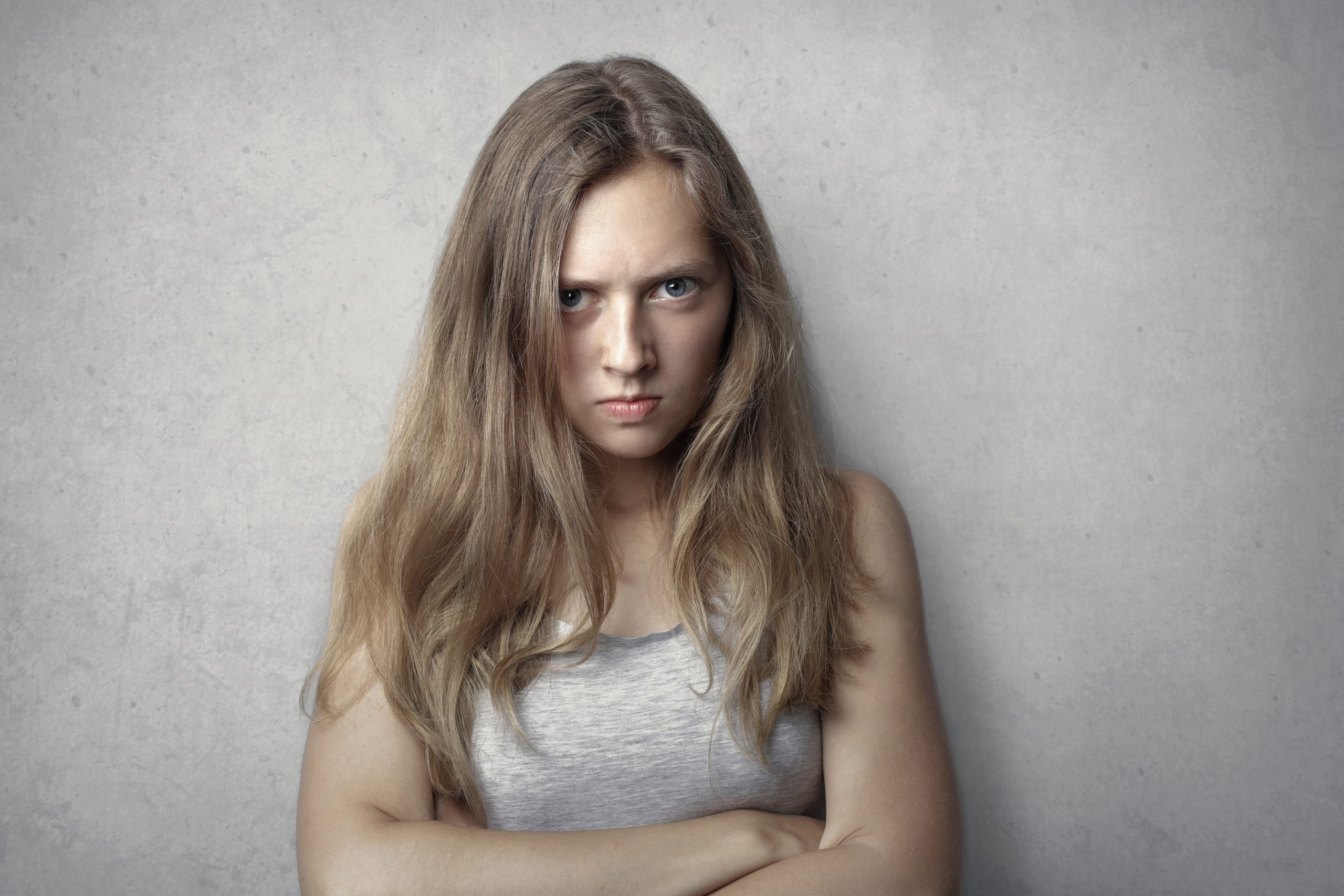 Angry woman with blonde hair and a gray tank top arms folded