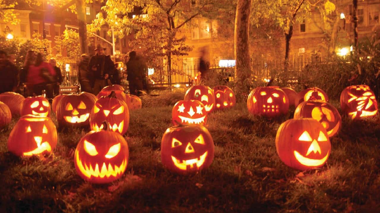 A bunch of carved and candlelit pumpkins in a city's public park at night